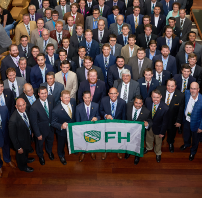 A group of FarmHouse men in suits, holding a flag with the FarmHouse crest