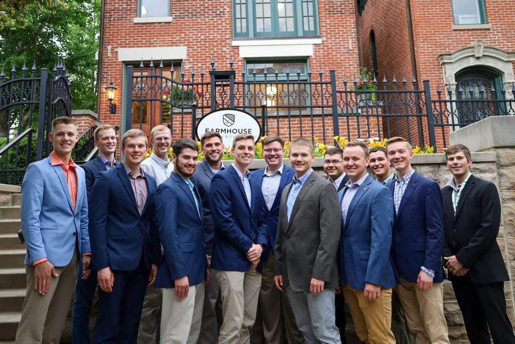 A group of FarmHouse men standing in front of the FarmHouse Fraternity headquarters office.