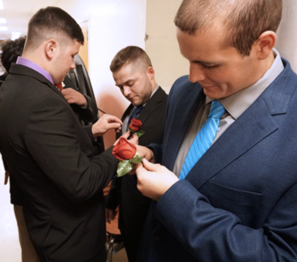 A group of FarmHouse men pinning roses to their suit jackets.